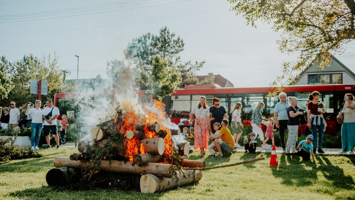 A lively community gathering enjoying a bonfire event outdoors on a sunny day.
