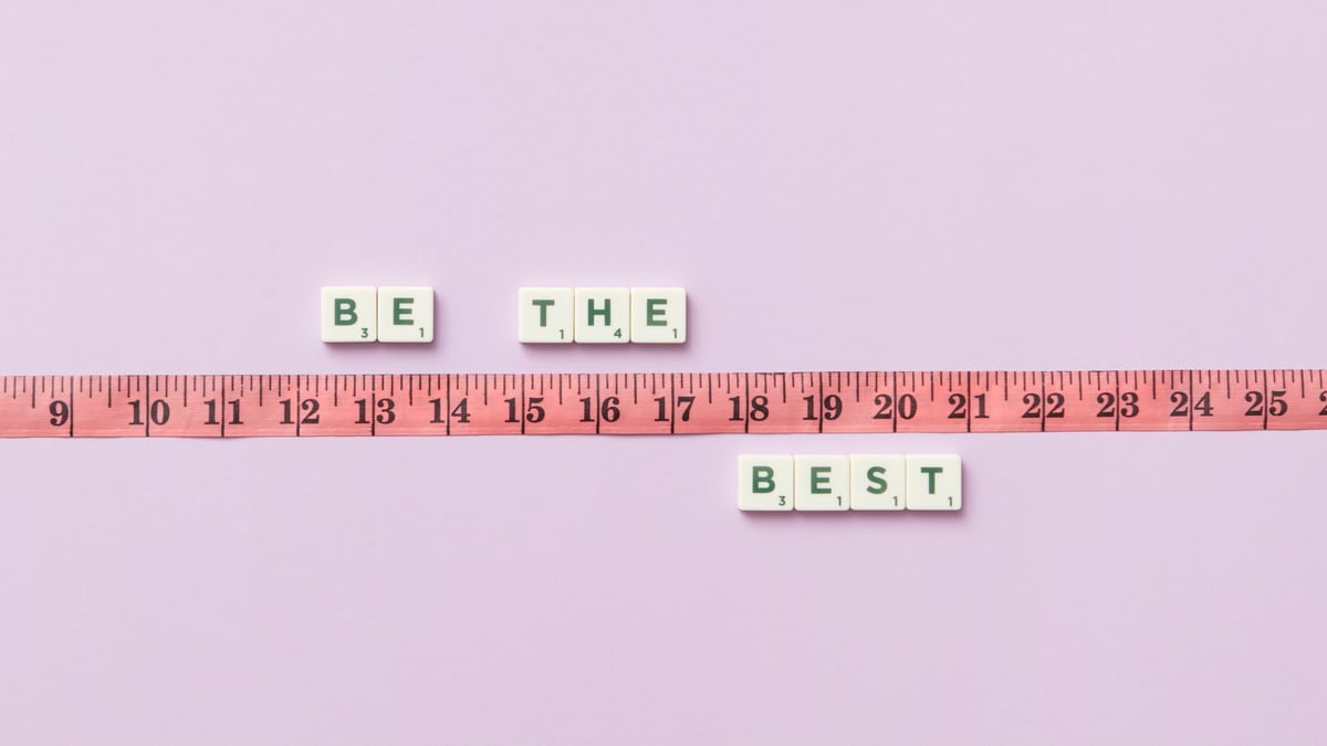 Scrabble tiles spell 'Be the Best' next to a measuring tape on a pastel background.